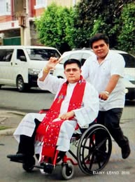 Fr. Arnold Abelardo seated in a wheelchair with another person standing behind him